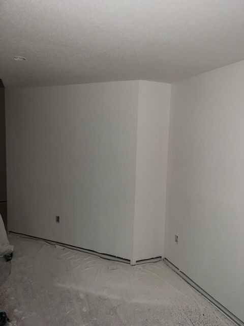 White-painted interior corner with a triangular wall section. Gray floor with painter's tape, white ceiling.