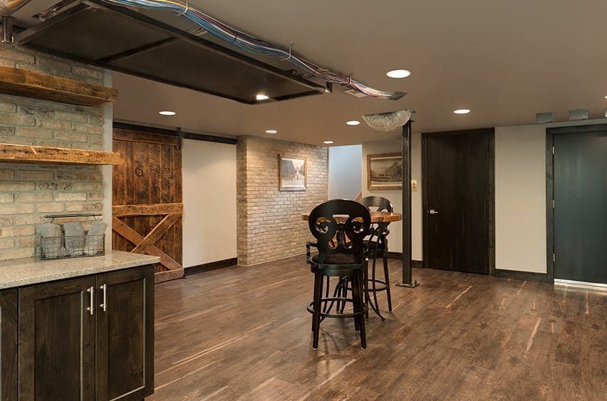Basement with bar area, brick walls, and dark wood accents. Includes stools and a sliding barn door.