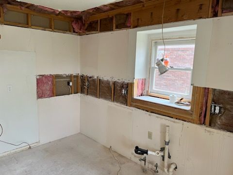 Kitchen undergoing renovation; exposed studs, partially removed wall, window, electrical and plumbing fixtures.