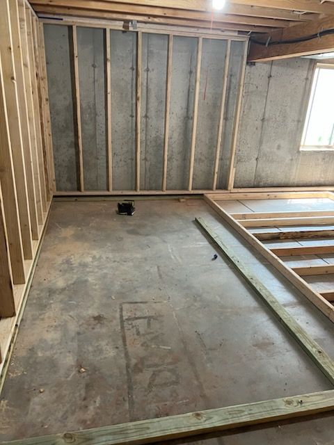 Framing a basement room: wood studs, concrete floor, and a window.