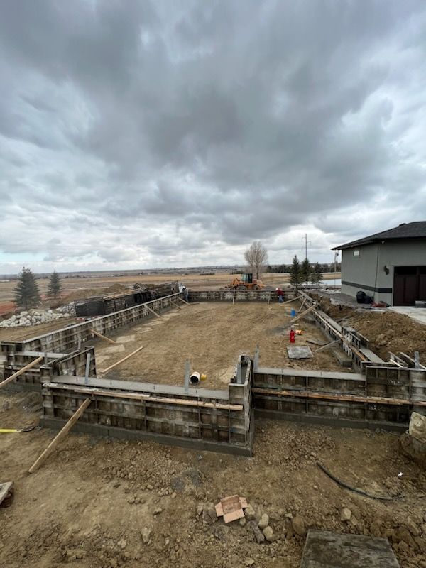 Construction site with gray concrete foundation forms set on brown dirt under cloudy sky.