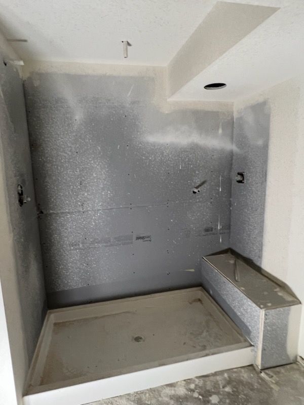A shower under construction with gray cement board walls, a shower pan, and a built-in bench.
