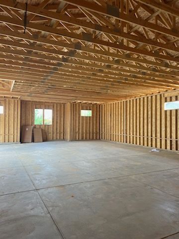 Interior of unfinished wooden-framed building with concrete floor and two small windows.
