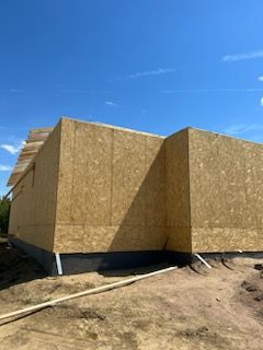 Construction site, exterior view of a partially built house with OSB sheathing on a sunny day.