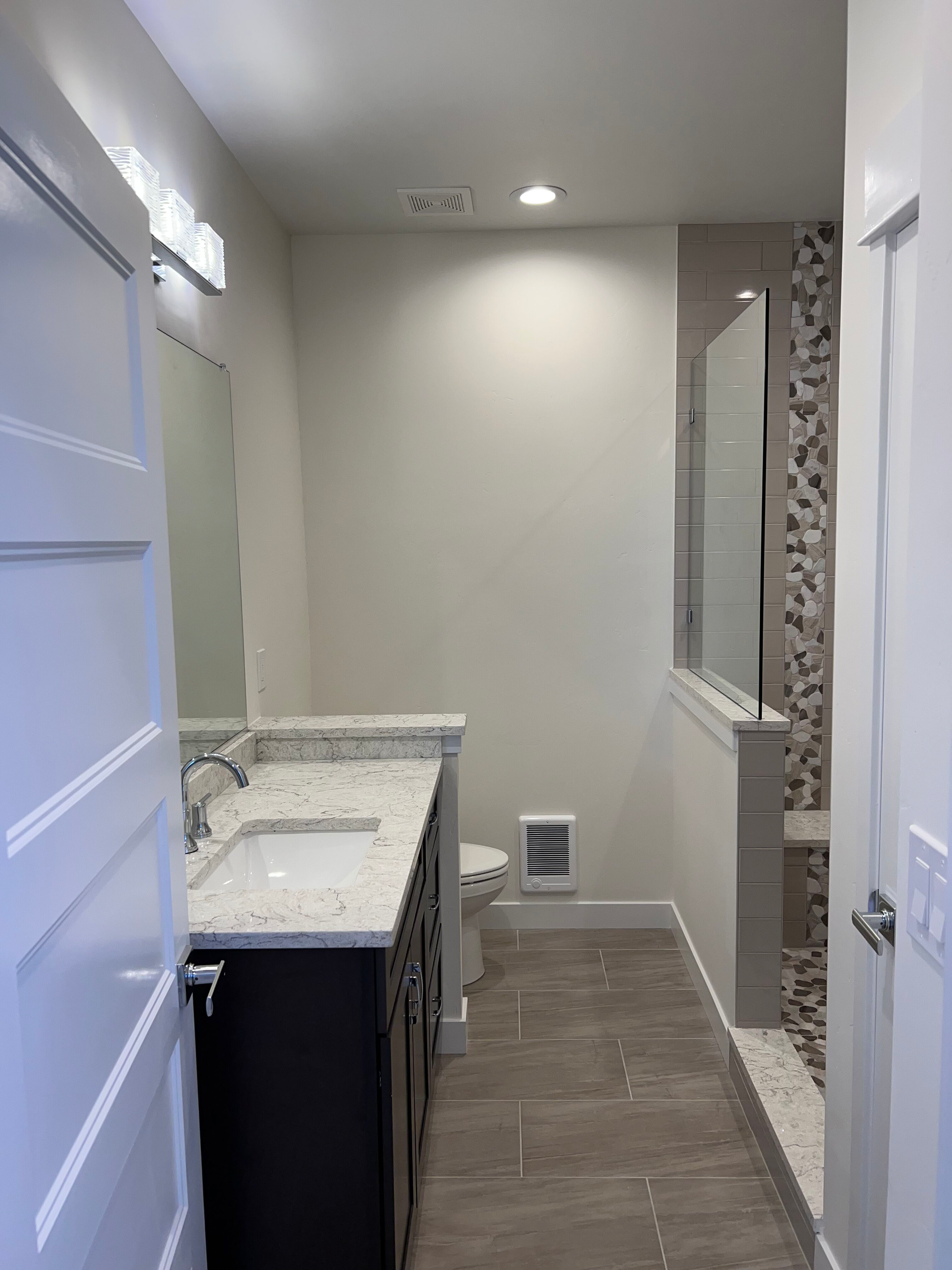 Bathroom with white walls, dark vanity, and stone shower. Door on the left.