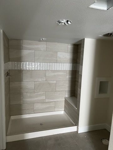 Shower stall with light beige tile, white bench, and accent band.