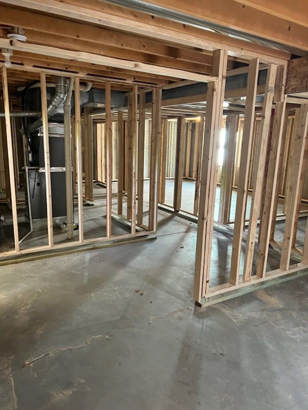 Basement room under construction: wooden framing, concrete floor, furnace, ductwork.