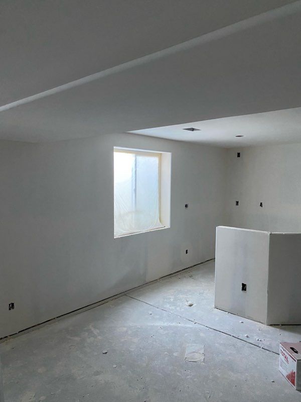 Unfinished room with a window, white walls, concrete floor, electrical outlets, and a square structure.
