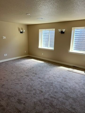 Empty room with beige walls, two windows, and dark gray carpet.