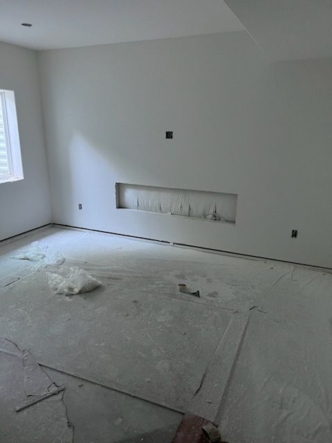 A white-walled room under construction, with a recessed wall feature.  Bare concrete floor, window with blinds.