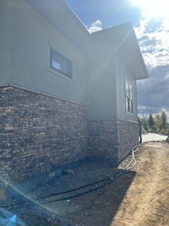 Exterior view of a house with stone veneer on the lower portion and green siding, under a bright sky.