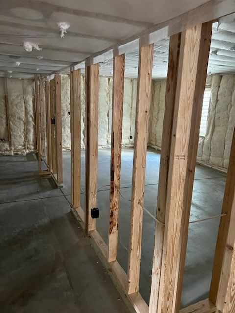 Interior framing of a room with exposed wooden studs, concrete floor, and insulated walls.