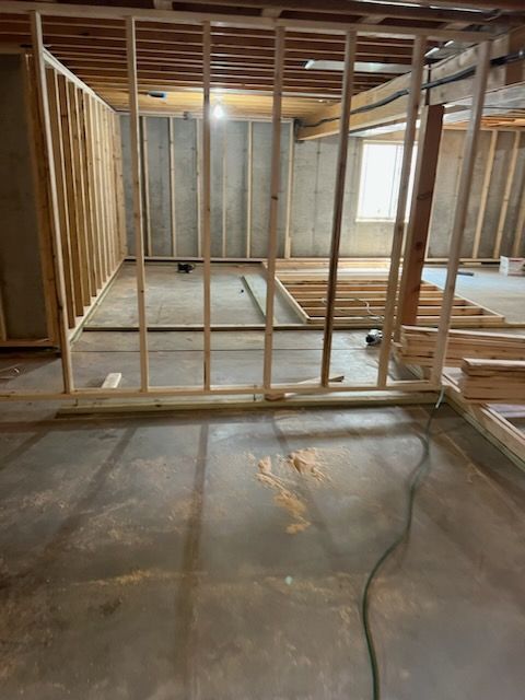 Basement under construction with wooden frames on a concrete floor; studs are up with a partial window.