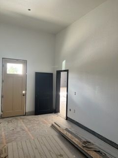 Interior of a room under construction with white walls, three doorways, and wooden flooring.