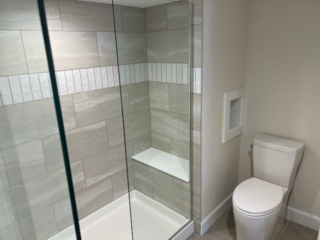 Modern bathroom with a glass shower, toilet, and neutral-toned tile.