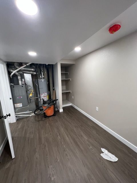 Basement room with wood-look floor, utility systems, shelving, and neutral walls.