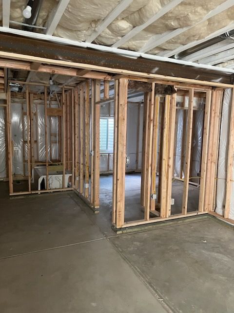 Framed walls in a basement, with concrete floor, insulation, and exposed ceiling beams, indicating a room under construction.