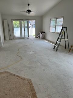 Empty room with a gray concrete floor, a ladder, and glass doors leading to a patio.