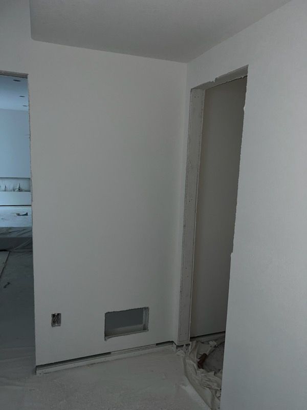 White painted interior walls with an open doorway, vent, and electrical outlet.