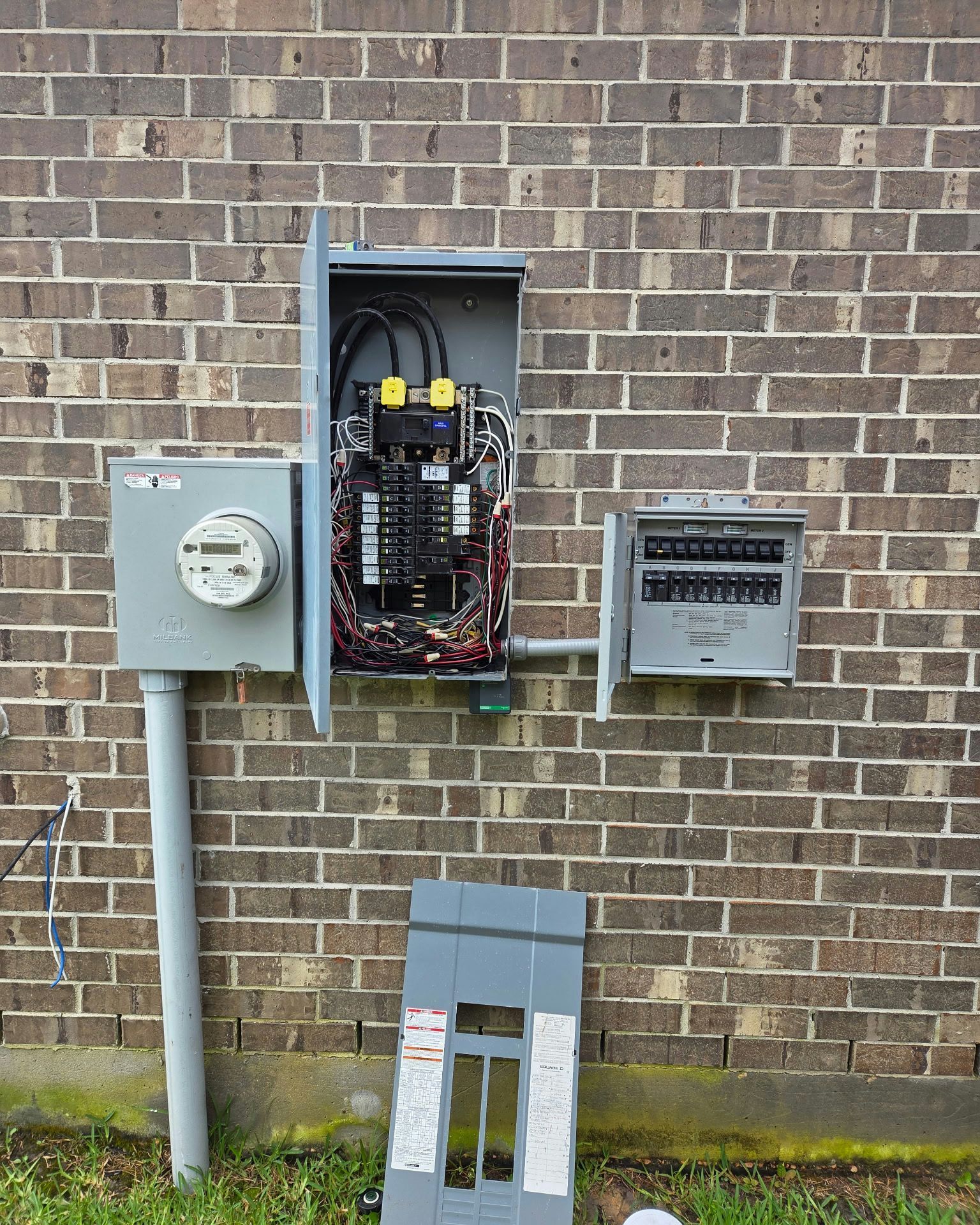 Electrical panel installation on brick wall; meter, main panel open, and subpanel.