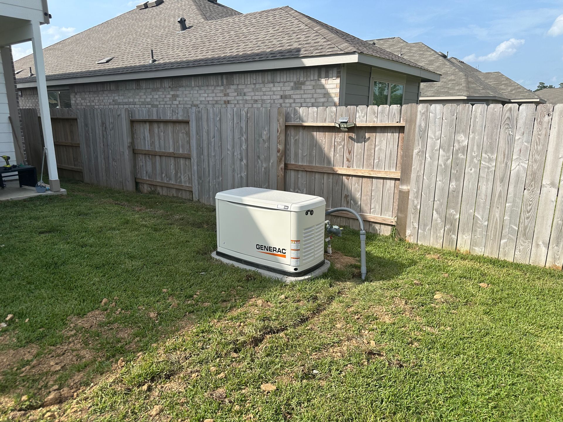 A standby generator in a backyard next to a wooden fence.