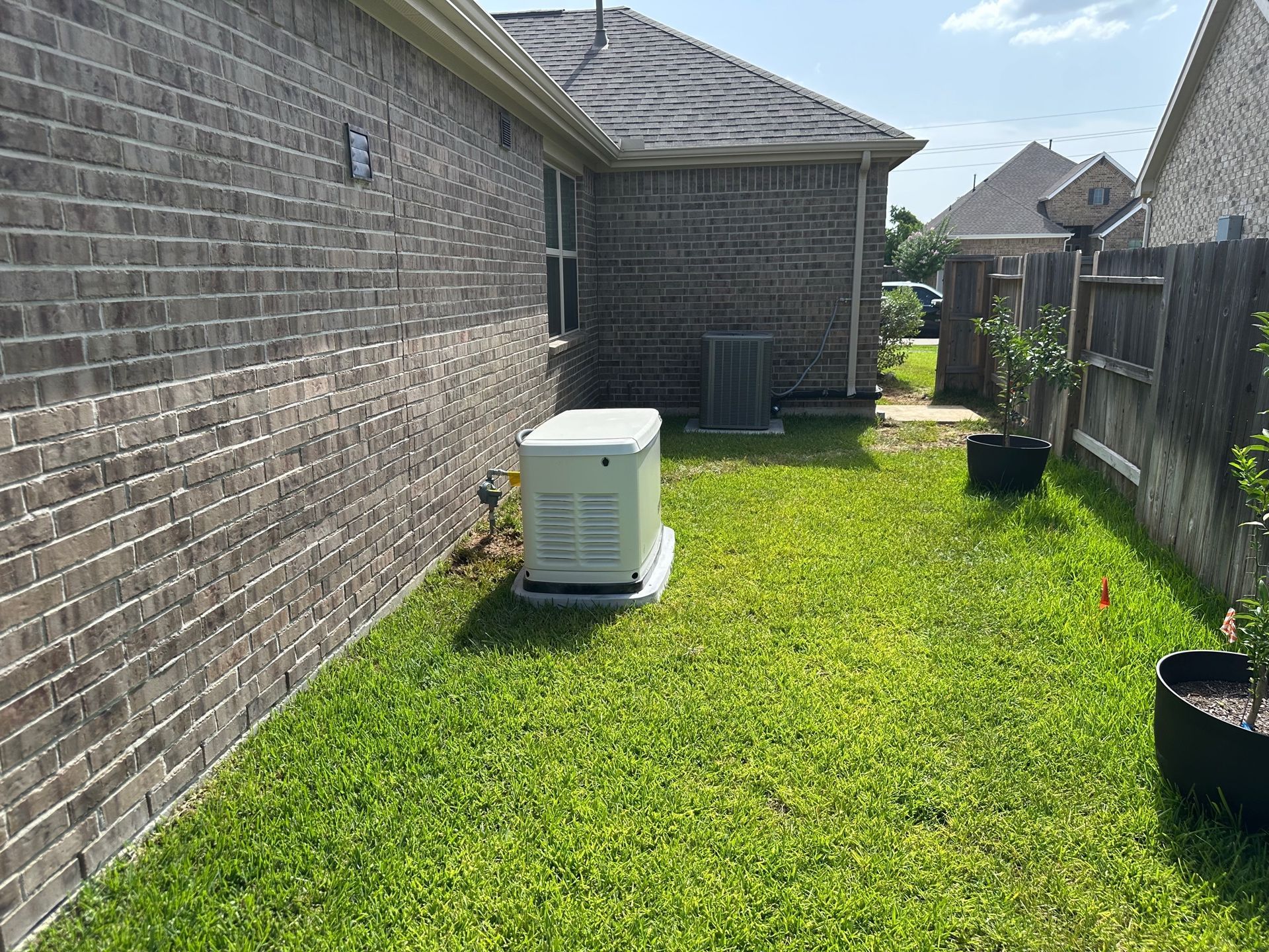 Generator on a grassy lawn next to a brick house and fence.