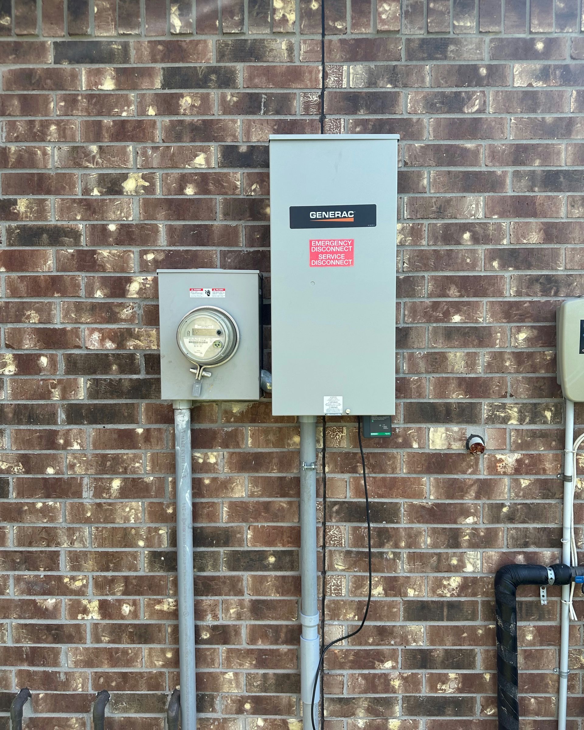 Electrical meter and panel on a brick wall. Gray boxes, silver conduits, black pipes.