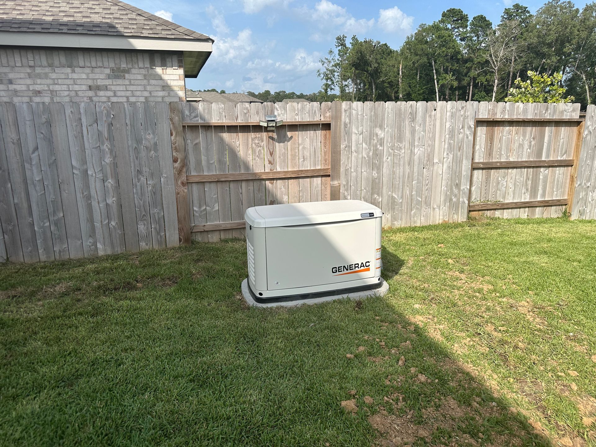 Generator in a backyard next to a wooden fence.