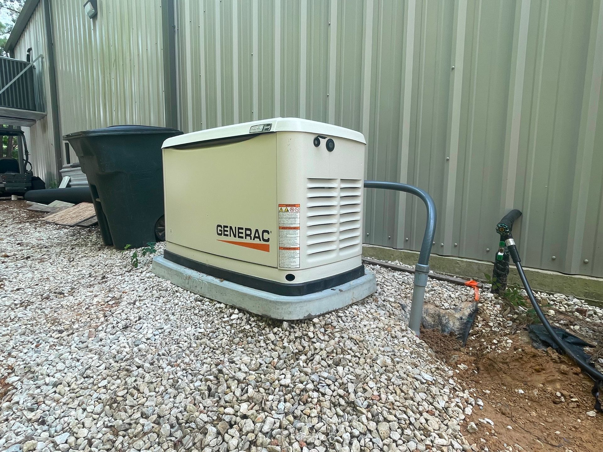 Tan Generac home generator on gravel next to a corrugated metal building.