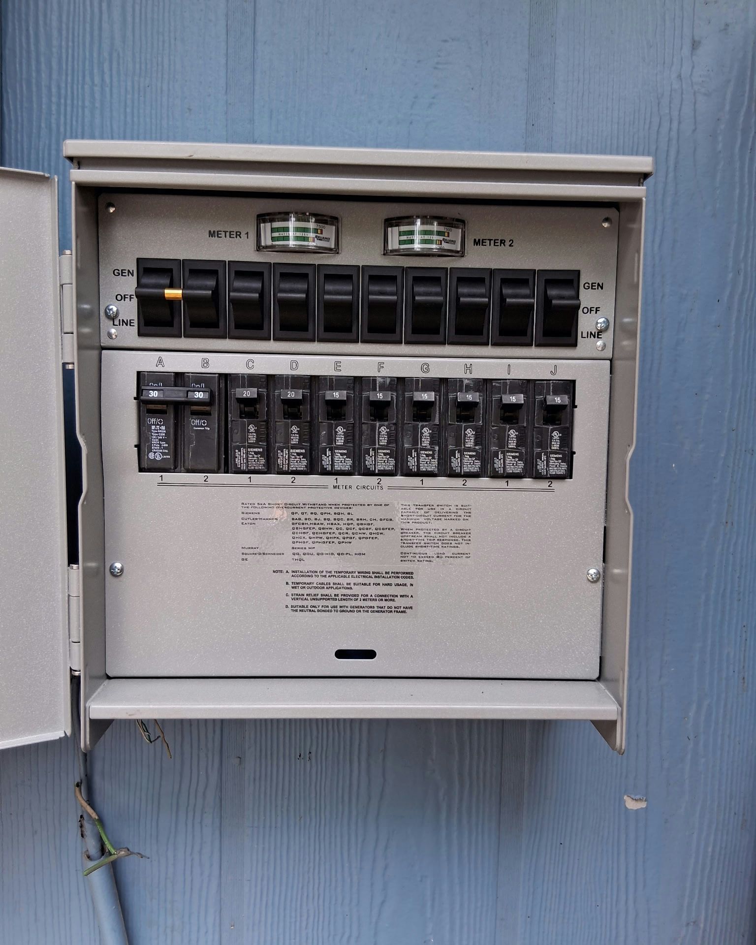 Gray electrical breaker box mounted on a blue wall. The box door is open, revealing multiple switches.