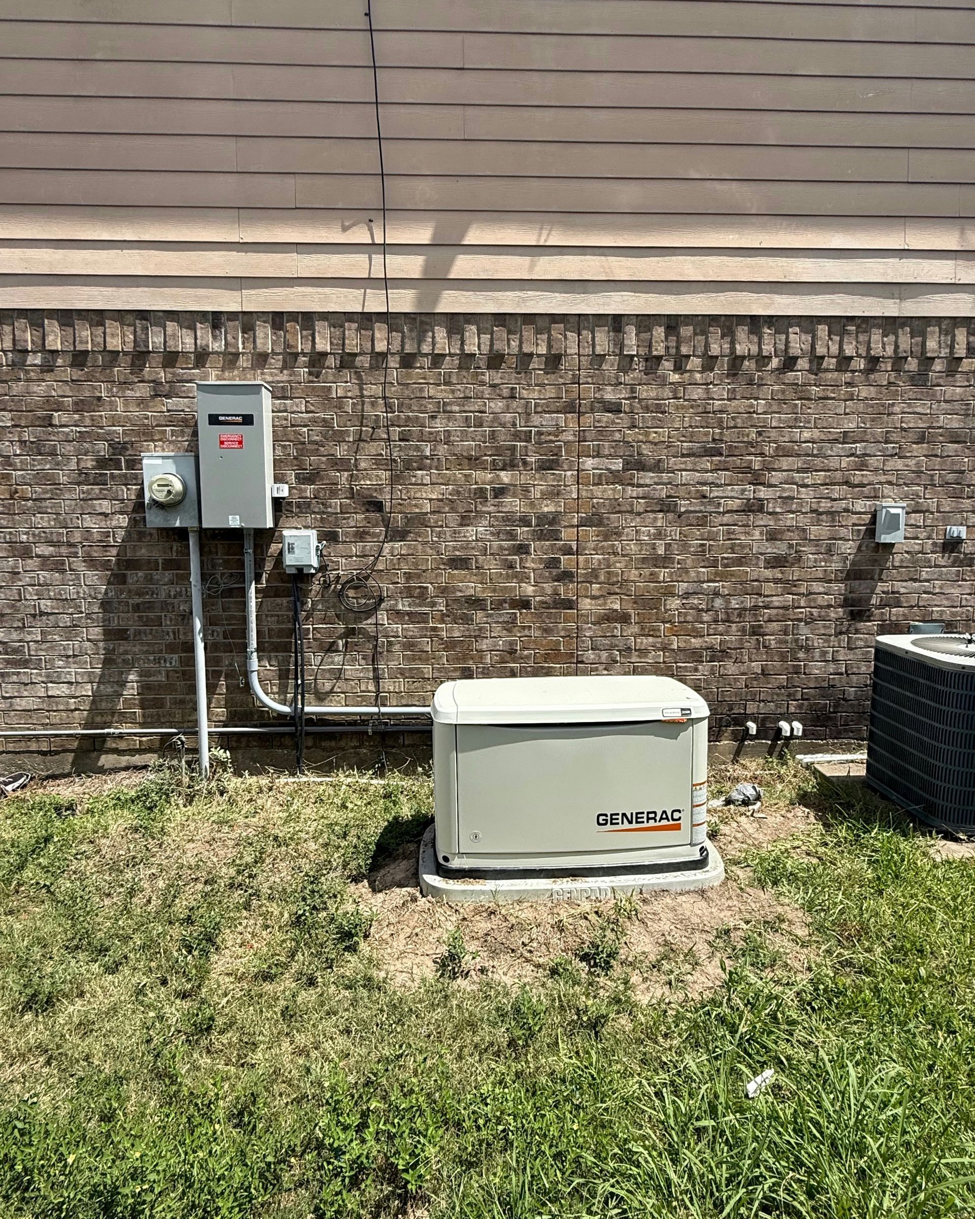 Generator and electrical box mounted on a brick wall, situated in a grassy yard.