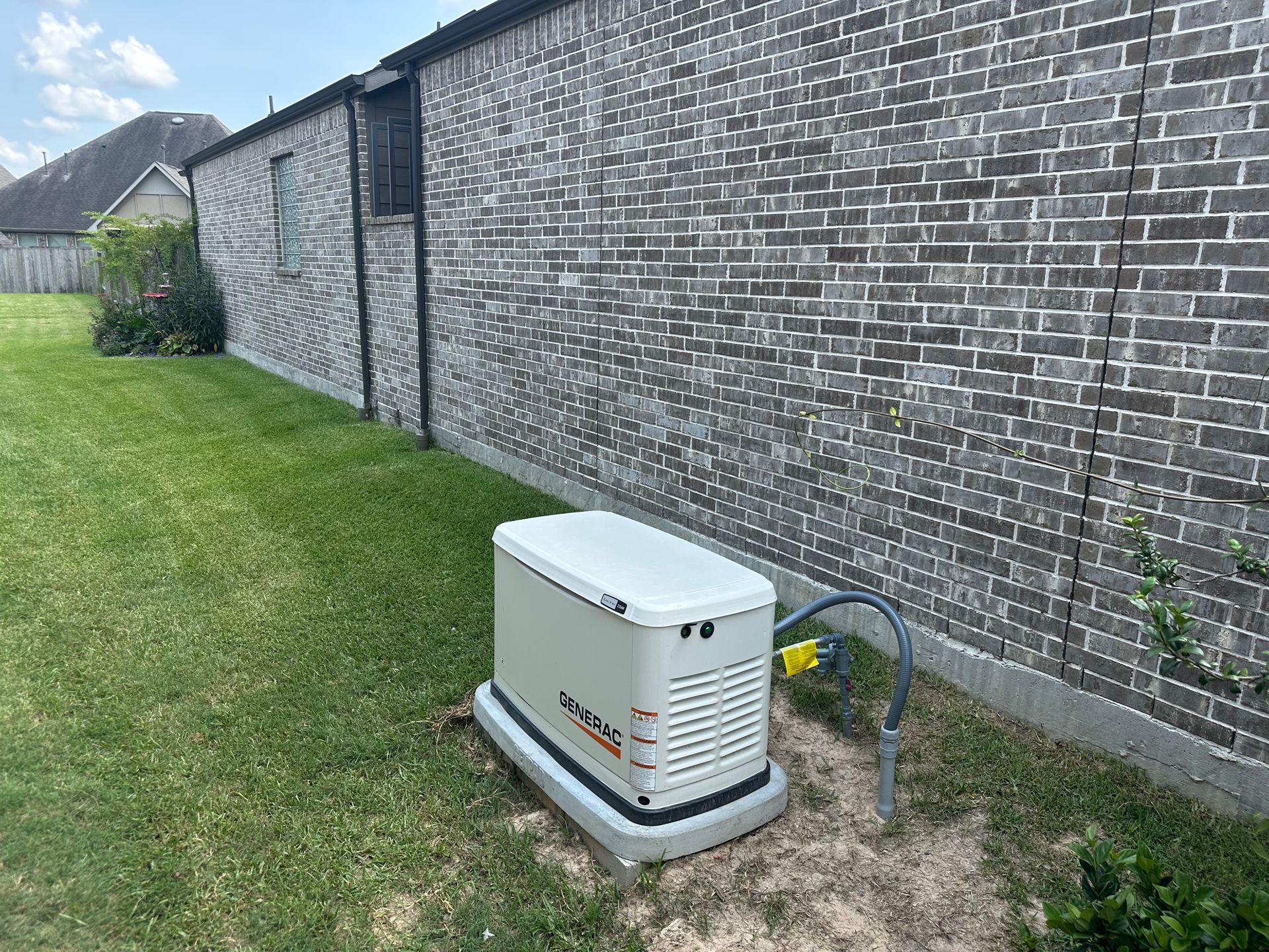 Generator on a concrete pad next to a gray brick wall in a grassy yard.
