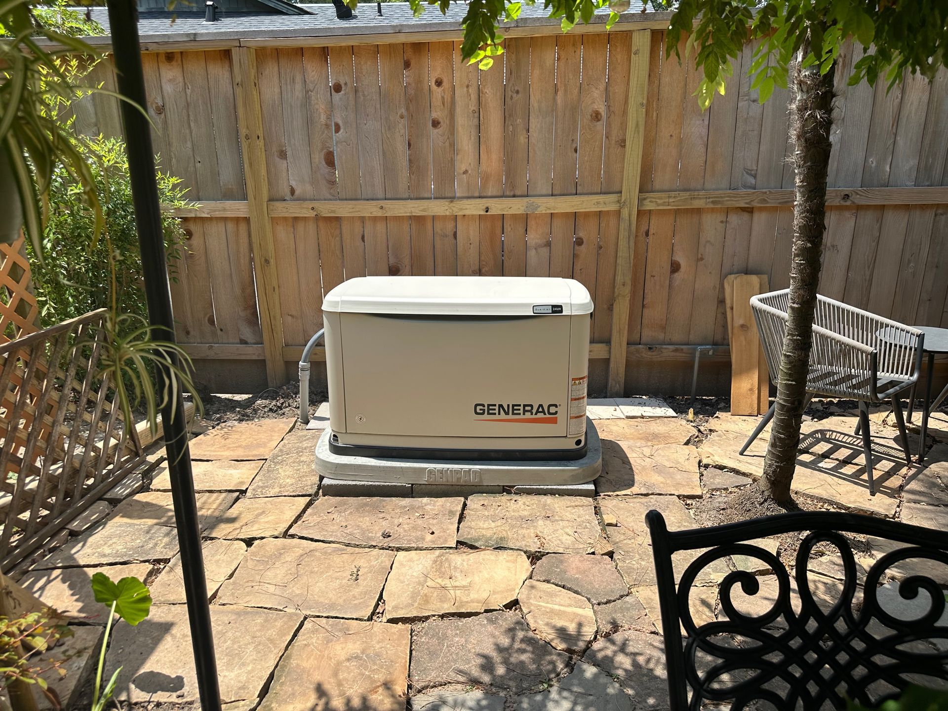 Tan generator on a concrete pad in a backyard, with a wooden fence and stone patio.