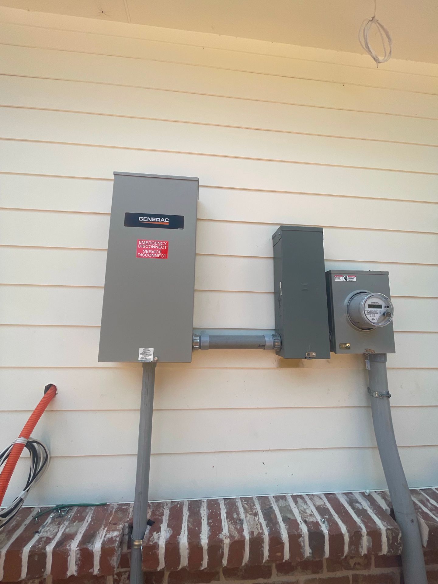 Exterior electrical boxes on a beige house wall: meter, disconnect, conduit, and breaker box.