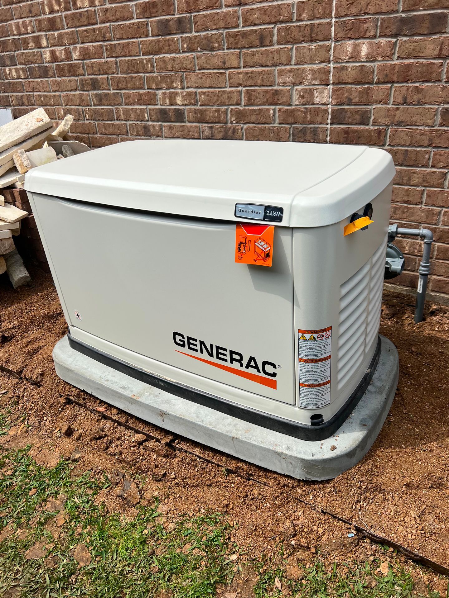 Generac home generator, tan color, on a concrete base, next to a brick wall.