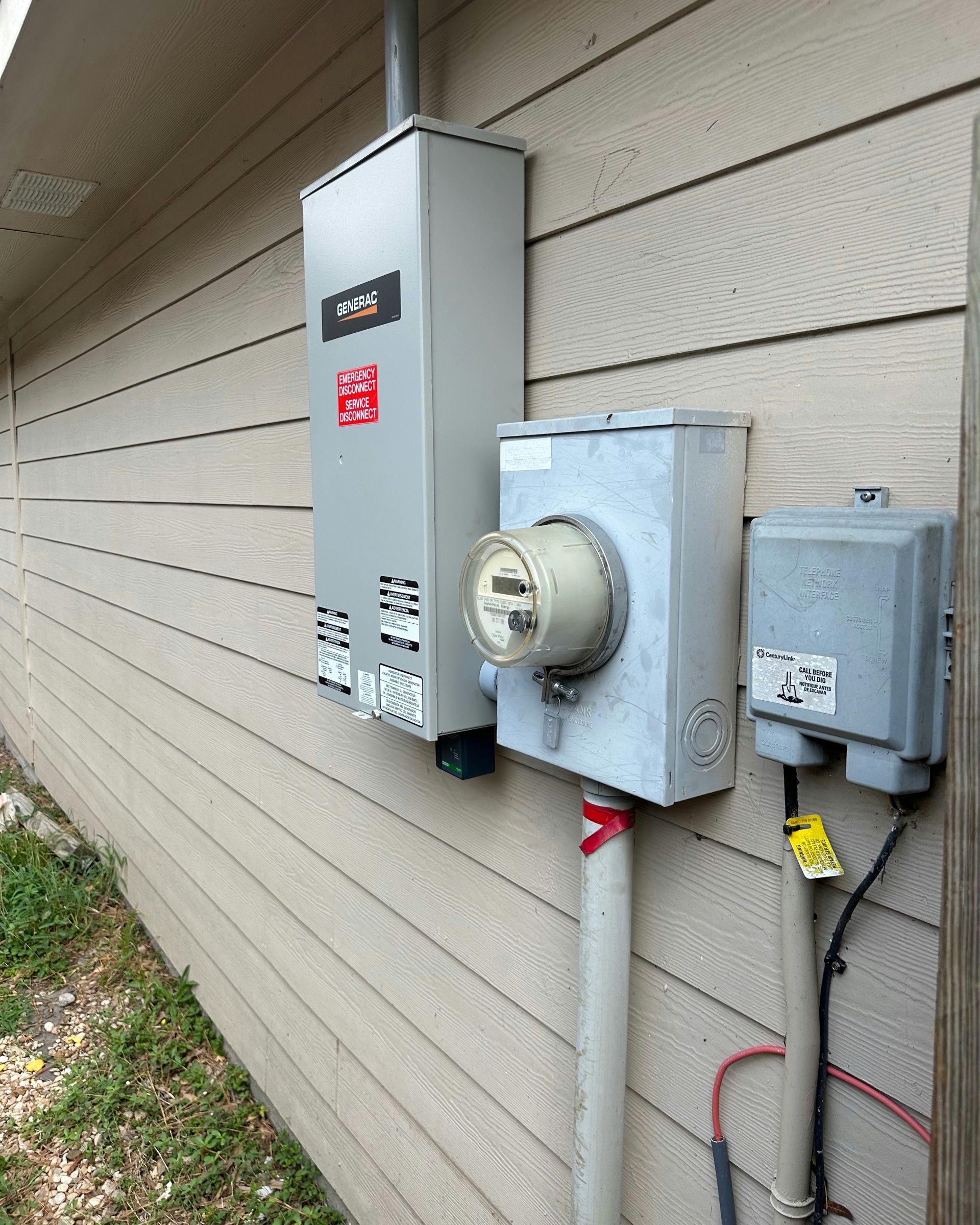 Electrical panel with meter and other components mounted on a tan siding exterior wall.