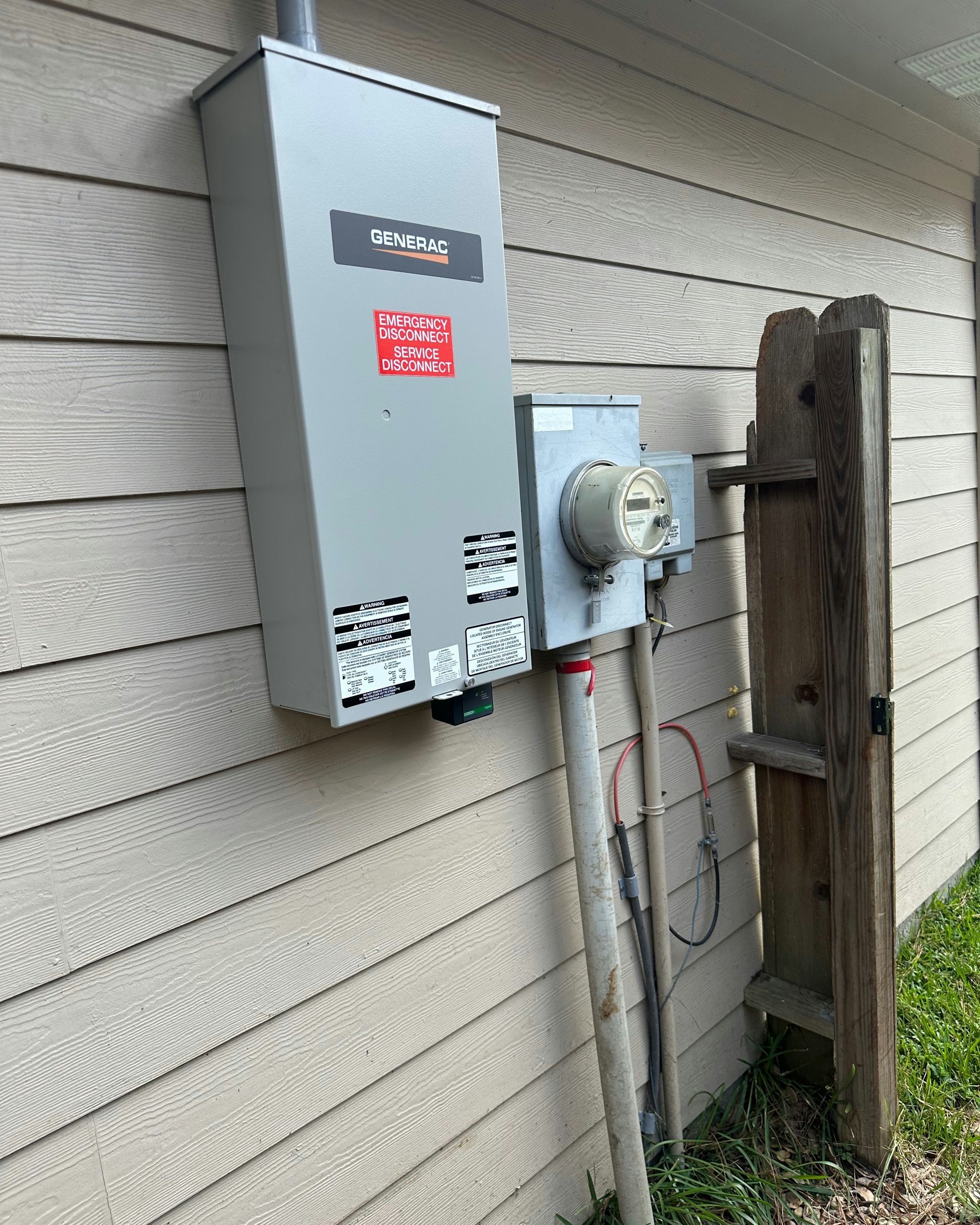 Gray electrical box and meter attached to a beige house, with conduit running down and a wooden ladder nearby.