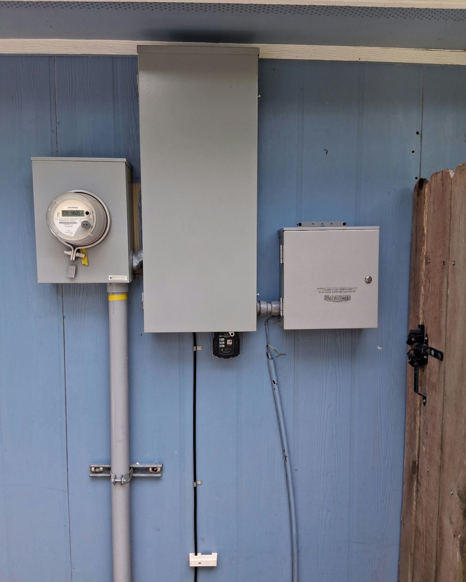 Electrical equipment mounted on a blue wall: meter box, panel, and a small box, with conduits and wiring.