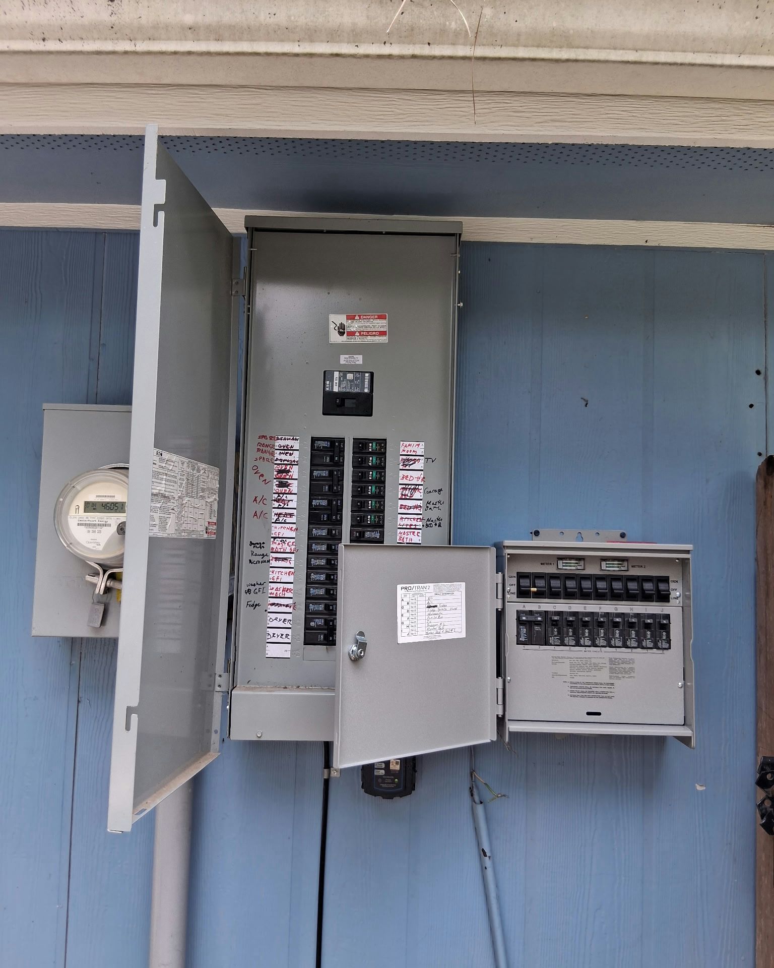Electrical panel on a blue building exterior, with open doors revealing circuit breakers and a meter.
