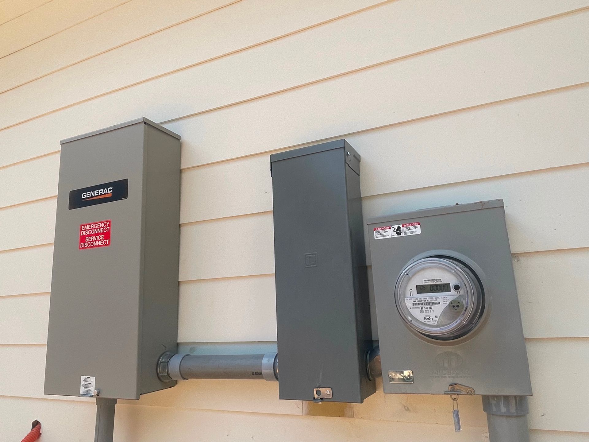 Gray electrical boxes and meter on a beige house exterior.