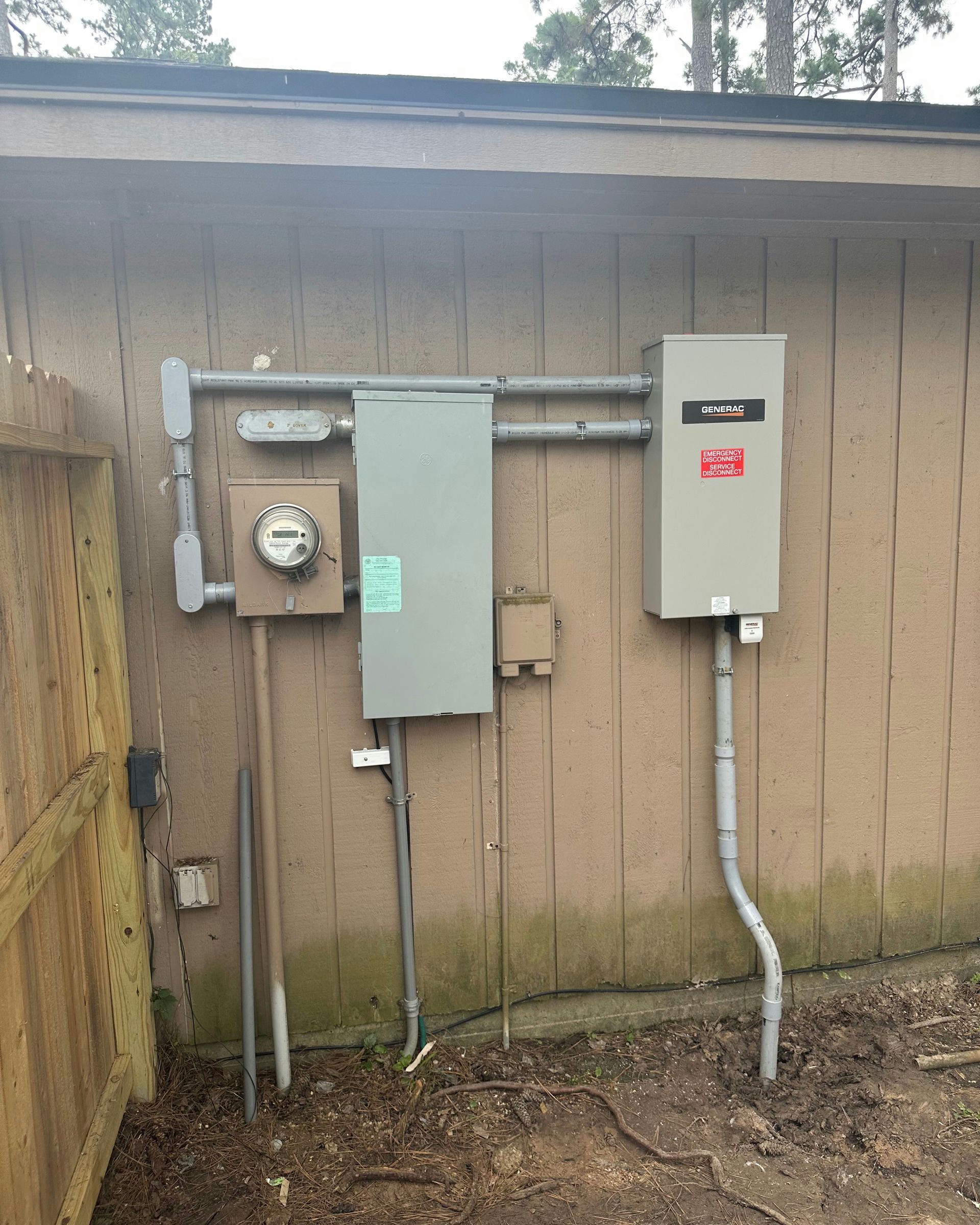 Exterior electrical panel components mounted on a wooden building. Includes meter, panel box, conduit, and ground rod.