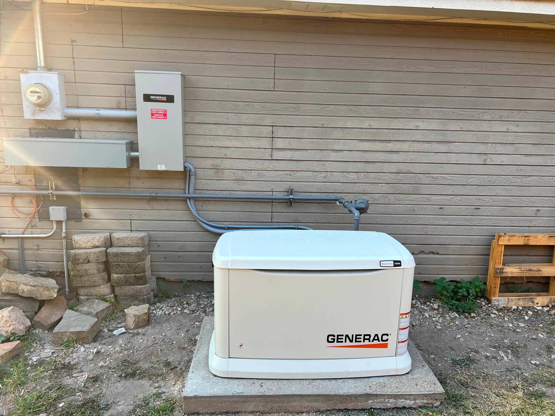 A Generac home generator is mounted on a concrete pad next to a beige building with electrical components.