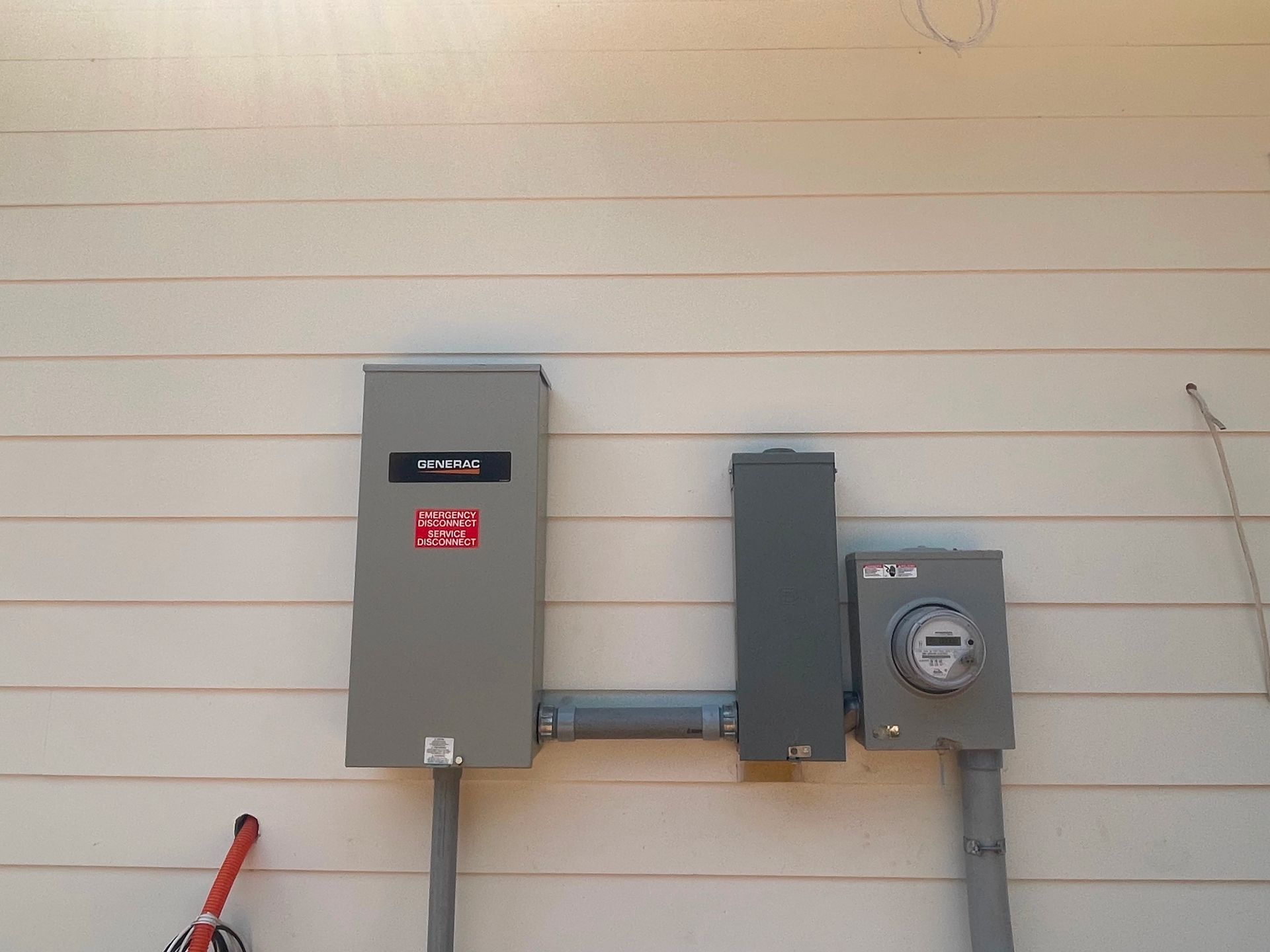 Electrical boxes on a cream-colored building exterior: a large grey box, a smaller grey box, and a box with a meter.