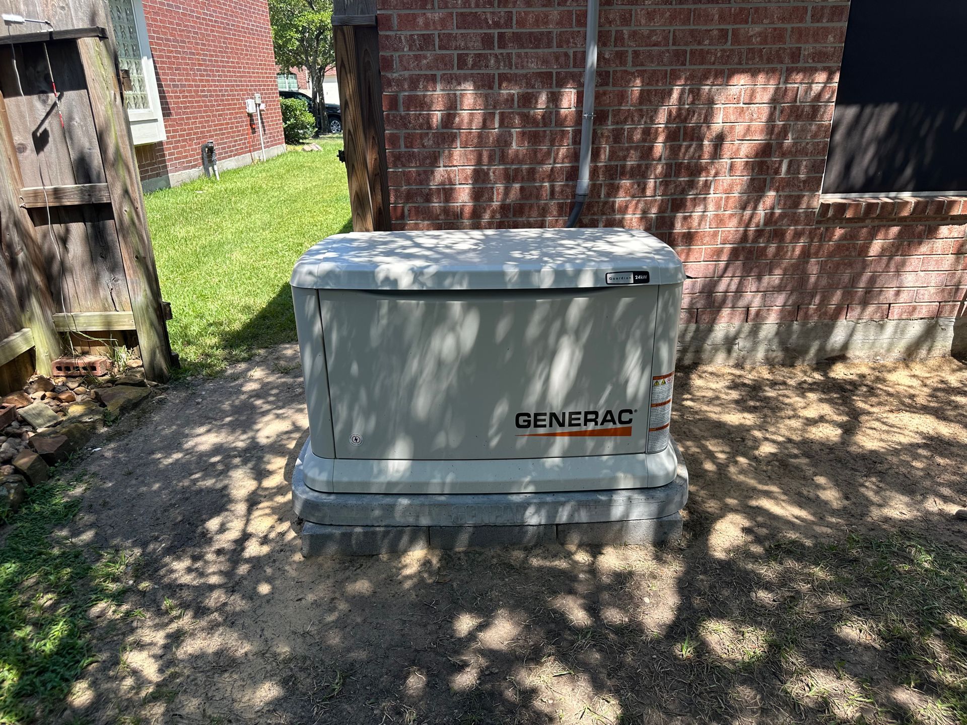A Generac generator outside, mounted on concrete blocks near a brick building and grass.