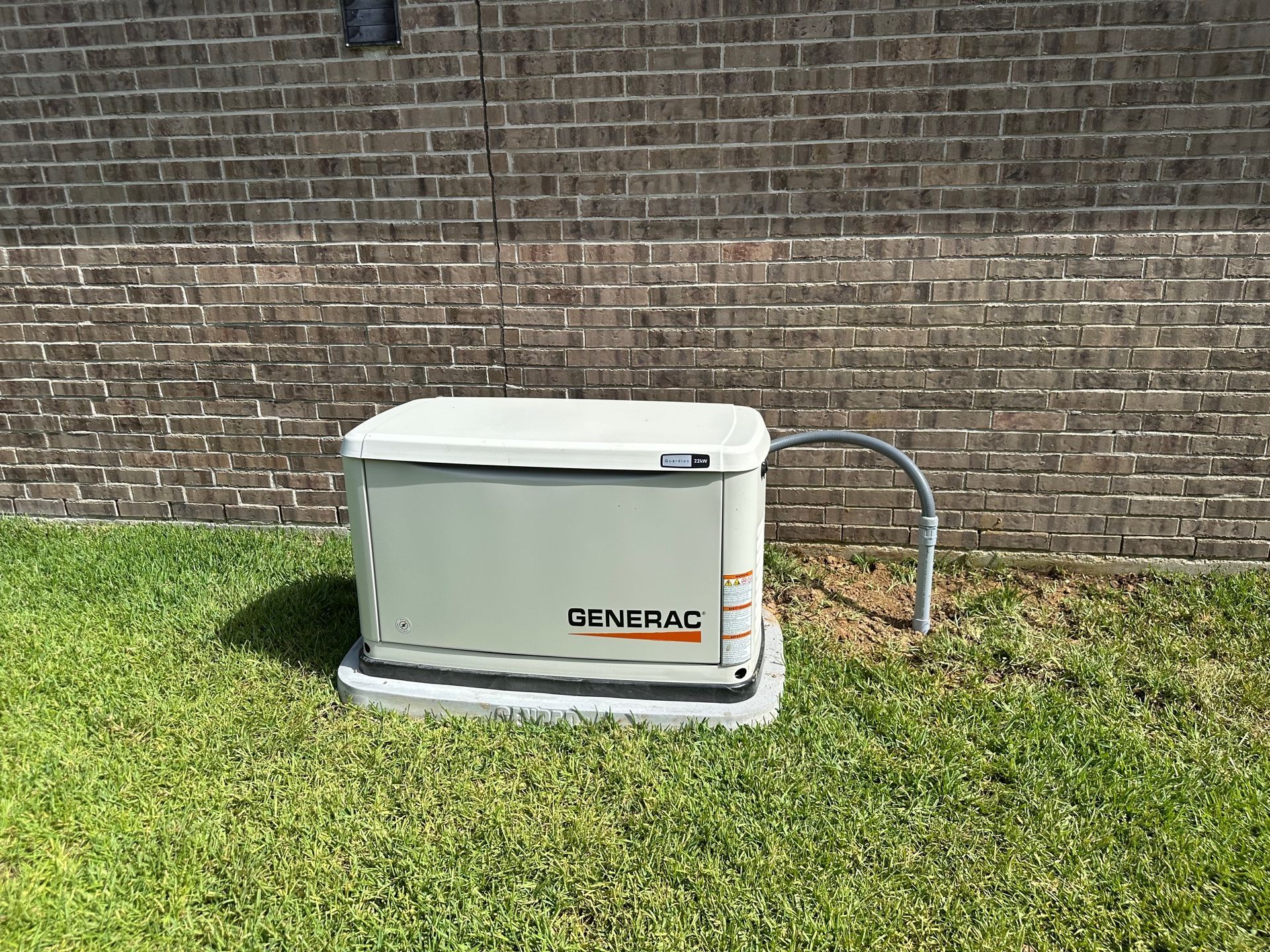 Generac generator on a concrete pad next to a brick wall and grass.