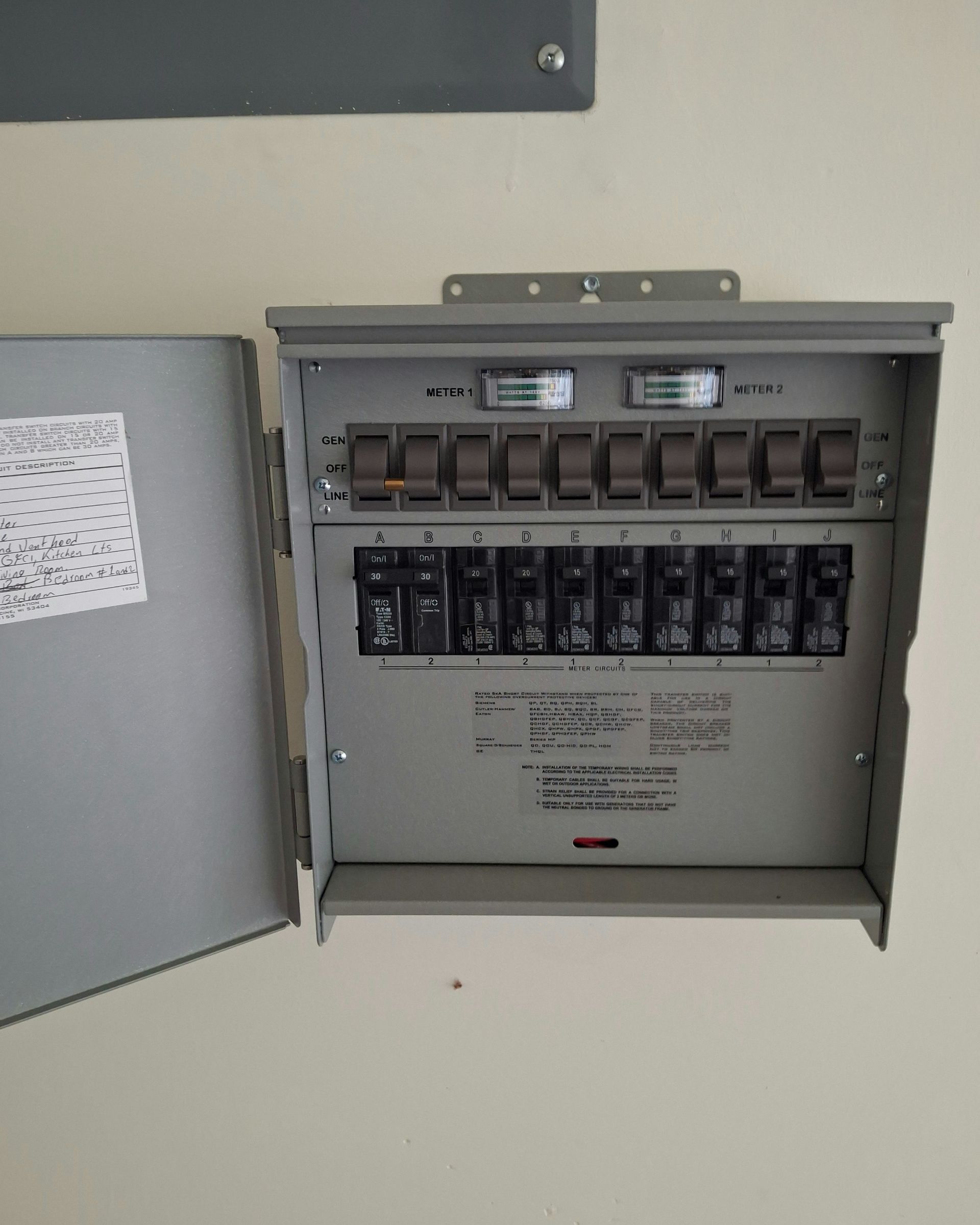 Gray electrical panel with open door, breakers visible. White wall.