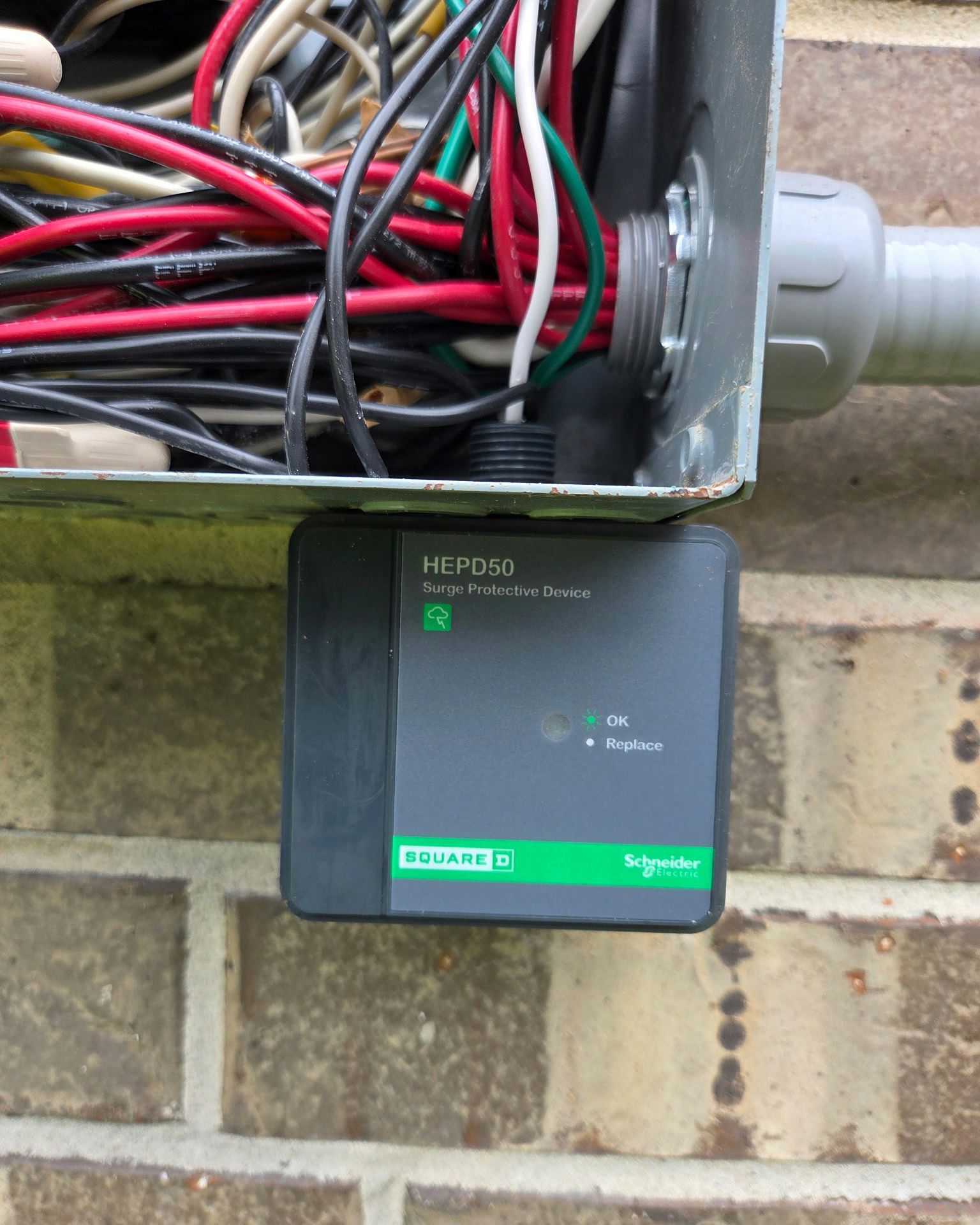 Electrical box with wires and a square, green Schneider Electric device attached to brick.