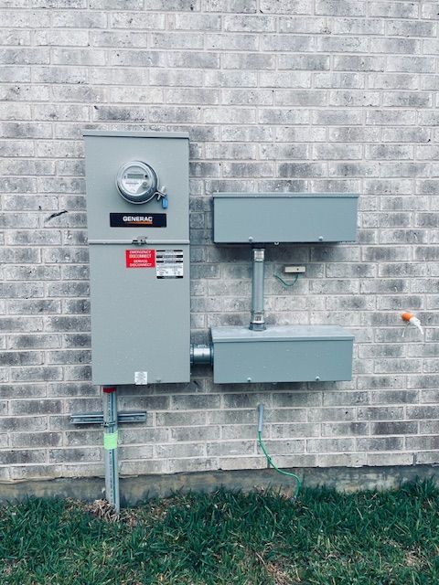 Gray electrical meter box and panels mounted on a gray brick wall, with green grounding wires and grass.