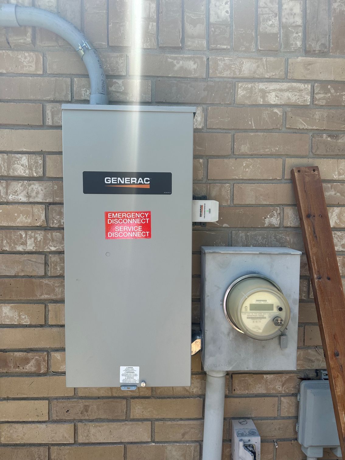 Exterior electrical panel and meter on a brick wall, likely for a backup generator.