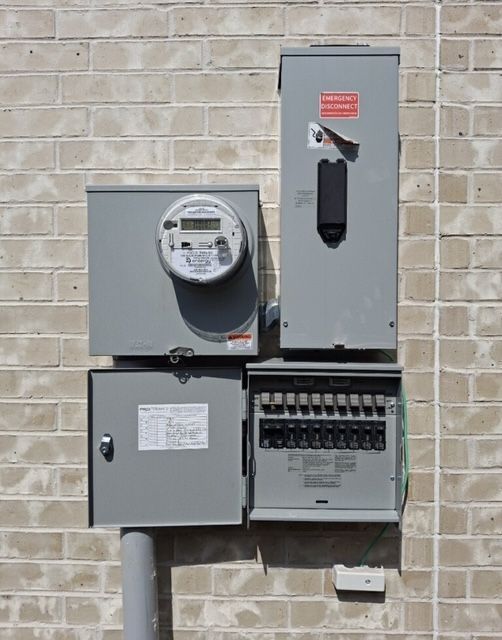 Exterior electrical panel on a brick wall, with a meter and circuit breakers.
